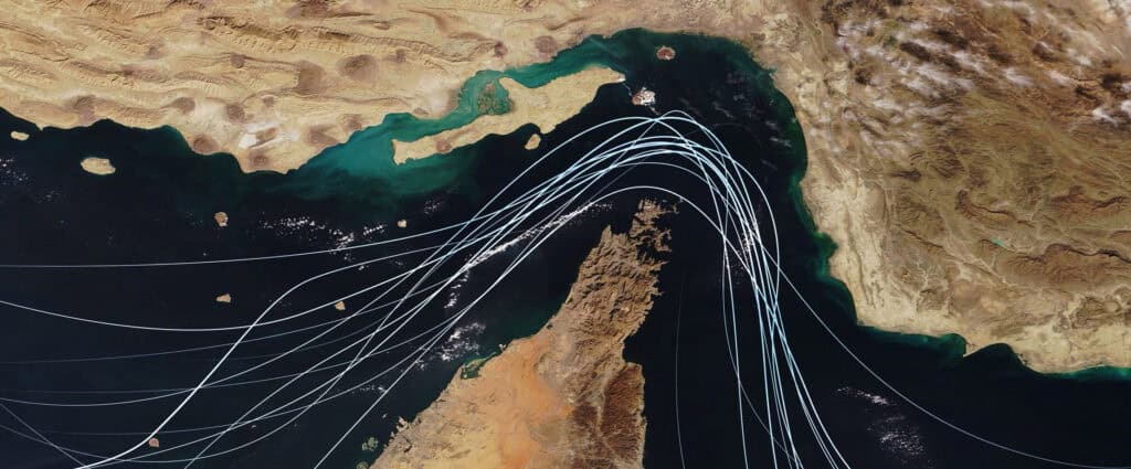 Satellite view of the Strait of Hormuz with white graphic lines representing global shipping lanes and maritime traffic between the Persian Gulf and Gulf of Oman. Strategic oil transport concept