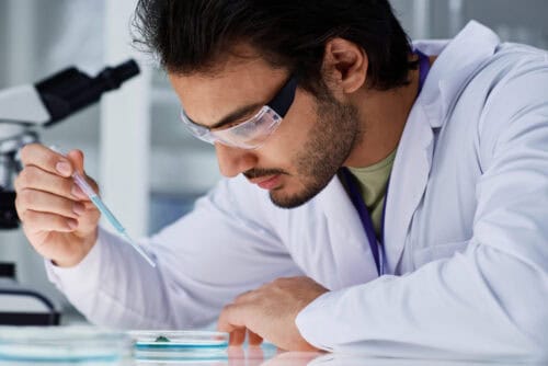 young serious man in eyeglasses and labcoat dropping liquid substance young serious man in eyeglasses and labcoat dropping liquid substance